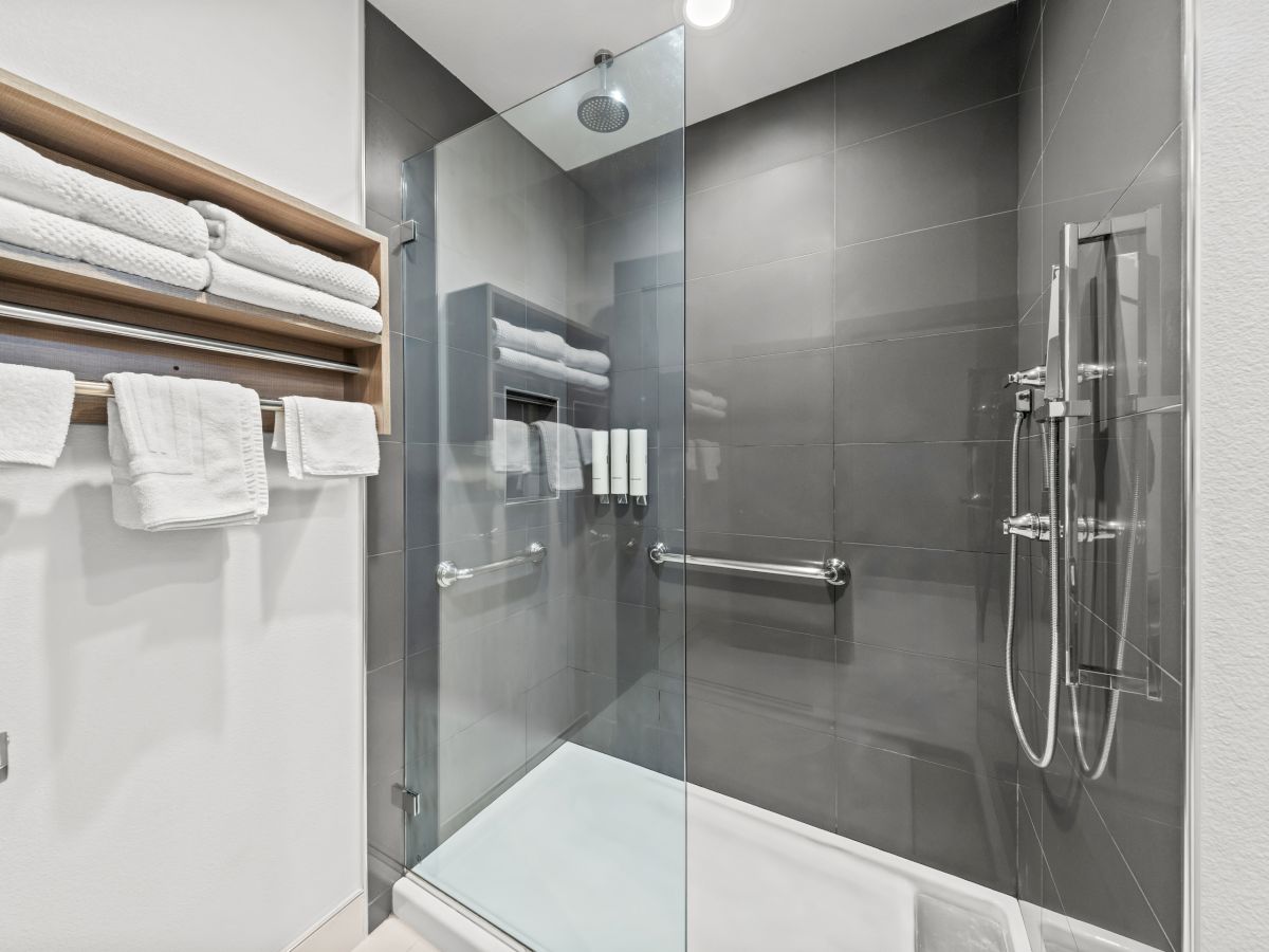 A modern bathroom with a glass shower, chrome fixtures, and neatly folded white towels in a wall rack.