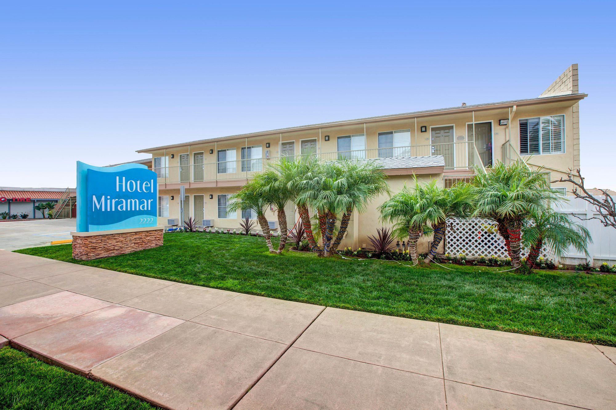 The image shows a two-story building with a sign reading "Hotel Miramar," surrounded by palm trees and a well-maintained lawn.