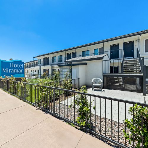 A sunny view of Hotel Miramar with balcony railings, potted plants, and a driveway in front.