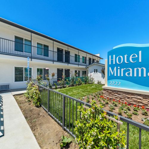 A sunny hotel courtyard with the sign &ldquo;Hotel Miramar&rdquo; and flower beds along a two-story building.