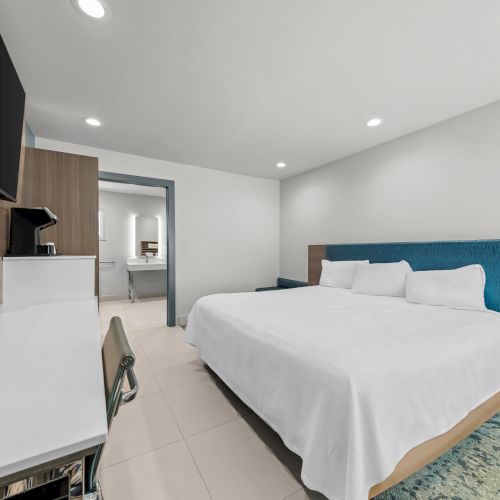 A modern hotel bedroom with a large bed, TV on a console, and a glimpse of a bathroom through a doorway.