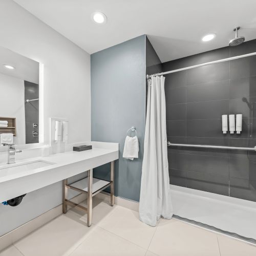 A modern bathroom with a countertop sink, tiled wall, and a walk-in shower with a rainfall showerhead and curtain.